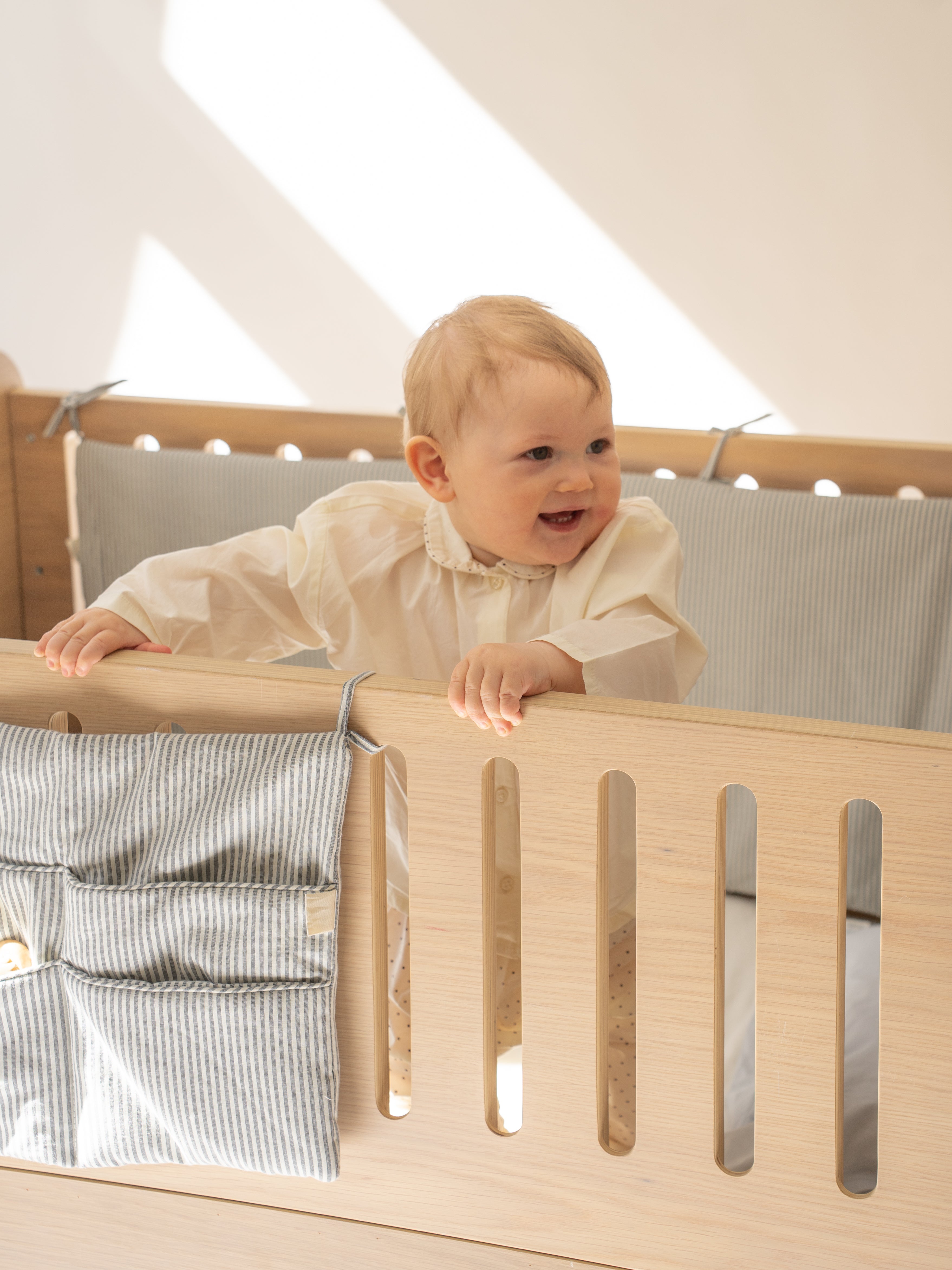 Baby standing in a crib with wooden sides and gray bedding.