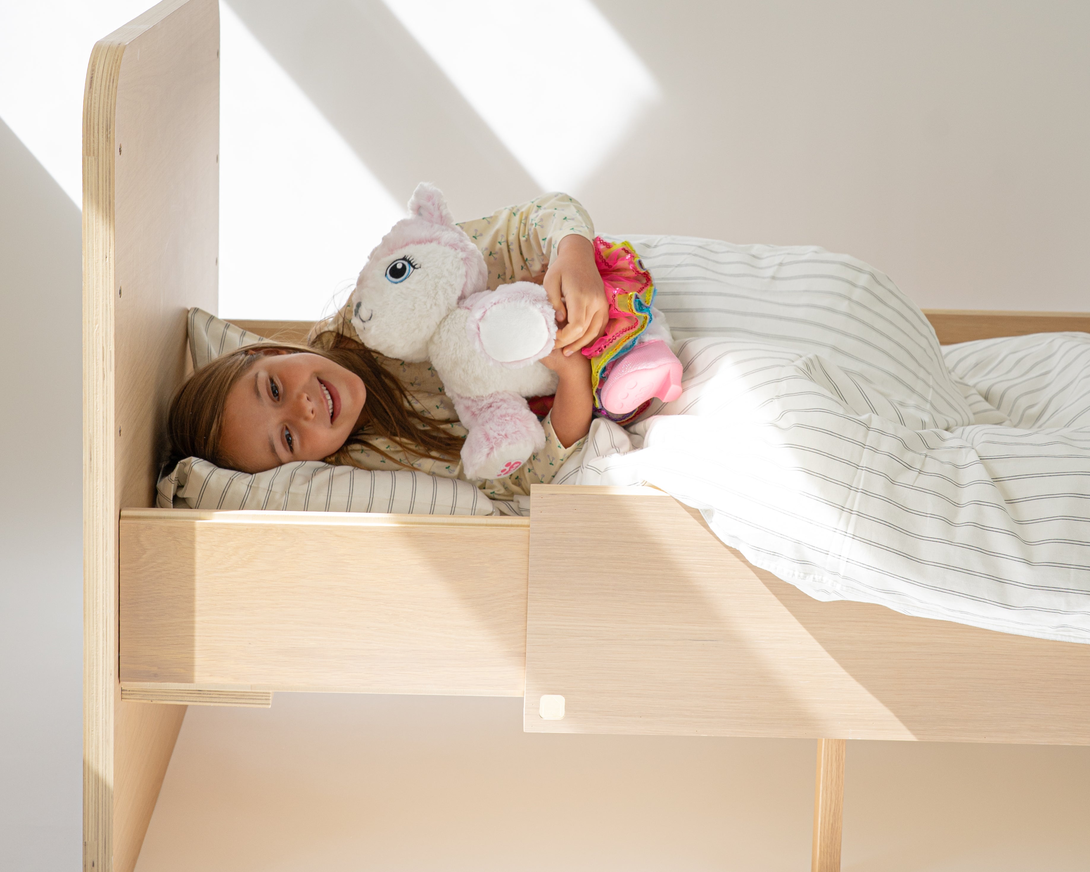 Child lying on a wooden bed with toys in a bright room