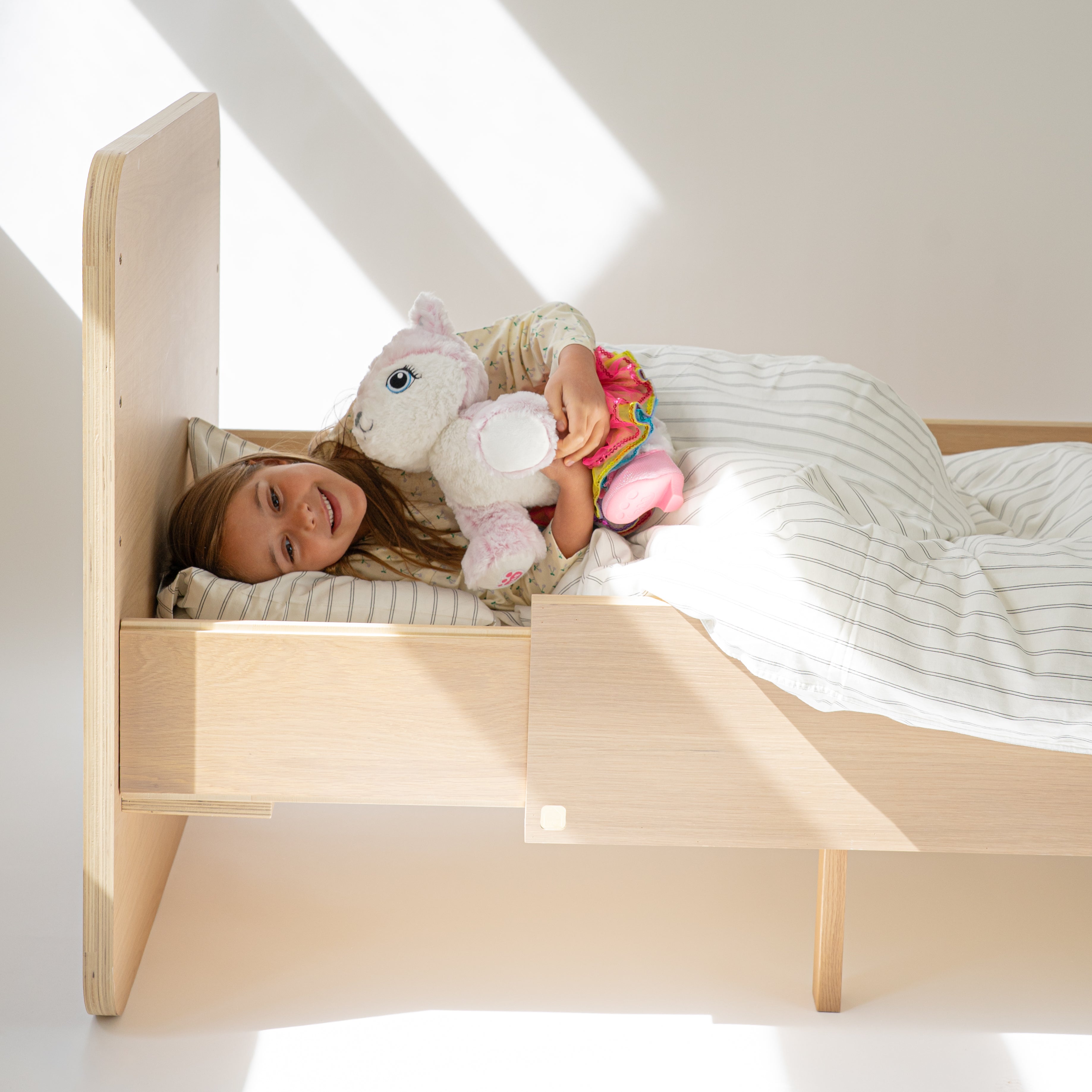 Child lying on a wooden bed with toys in a bright room