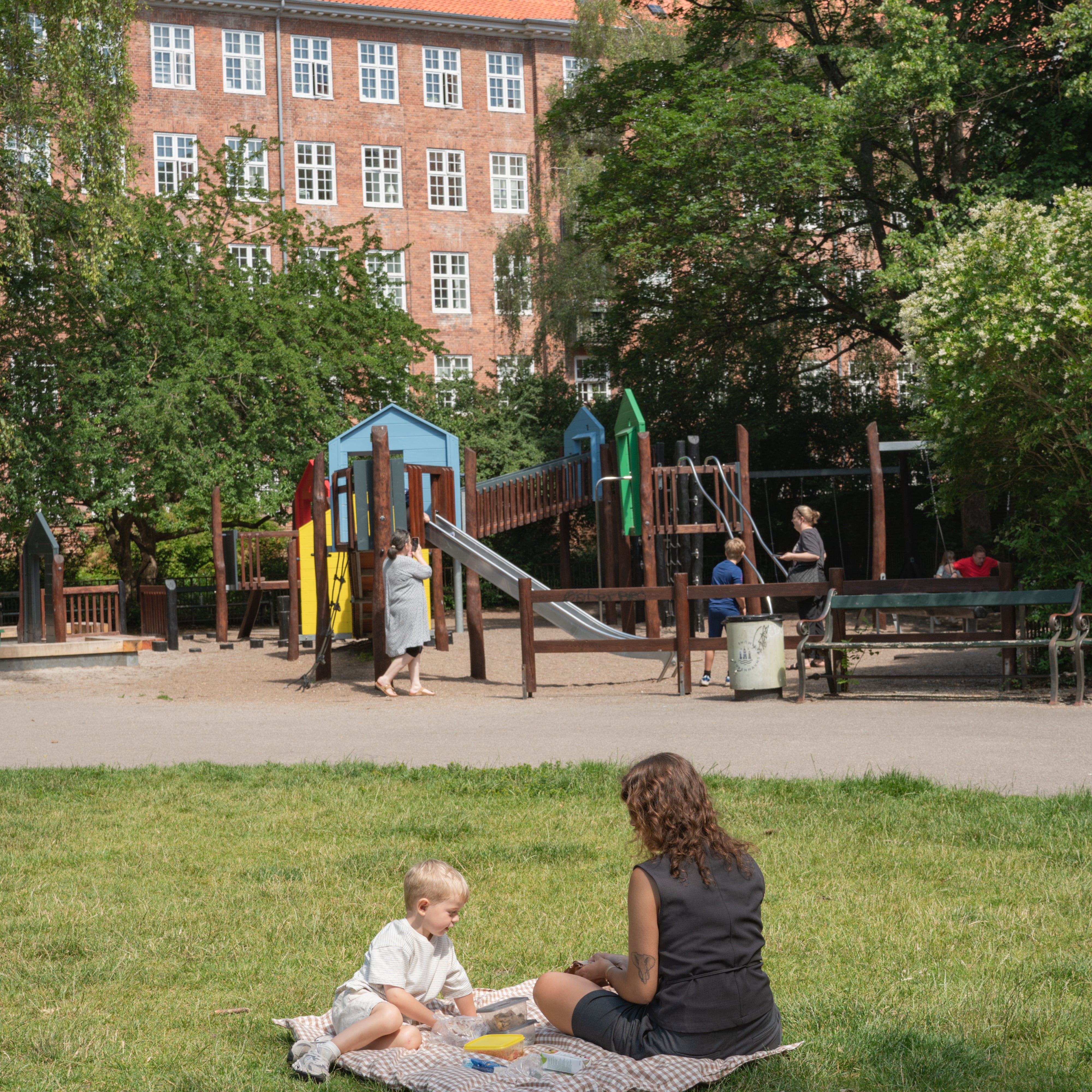 Woman and child sitting on a blanket in a park with playground in the background
