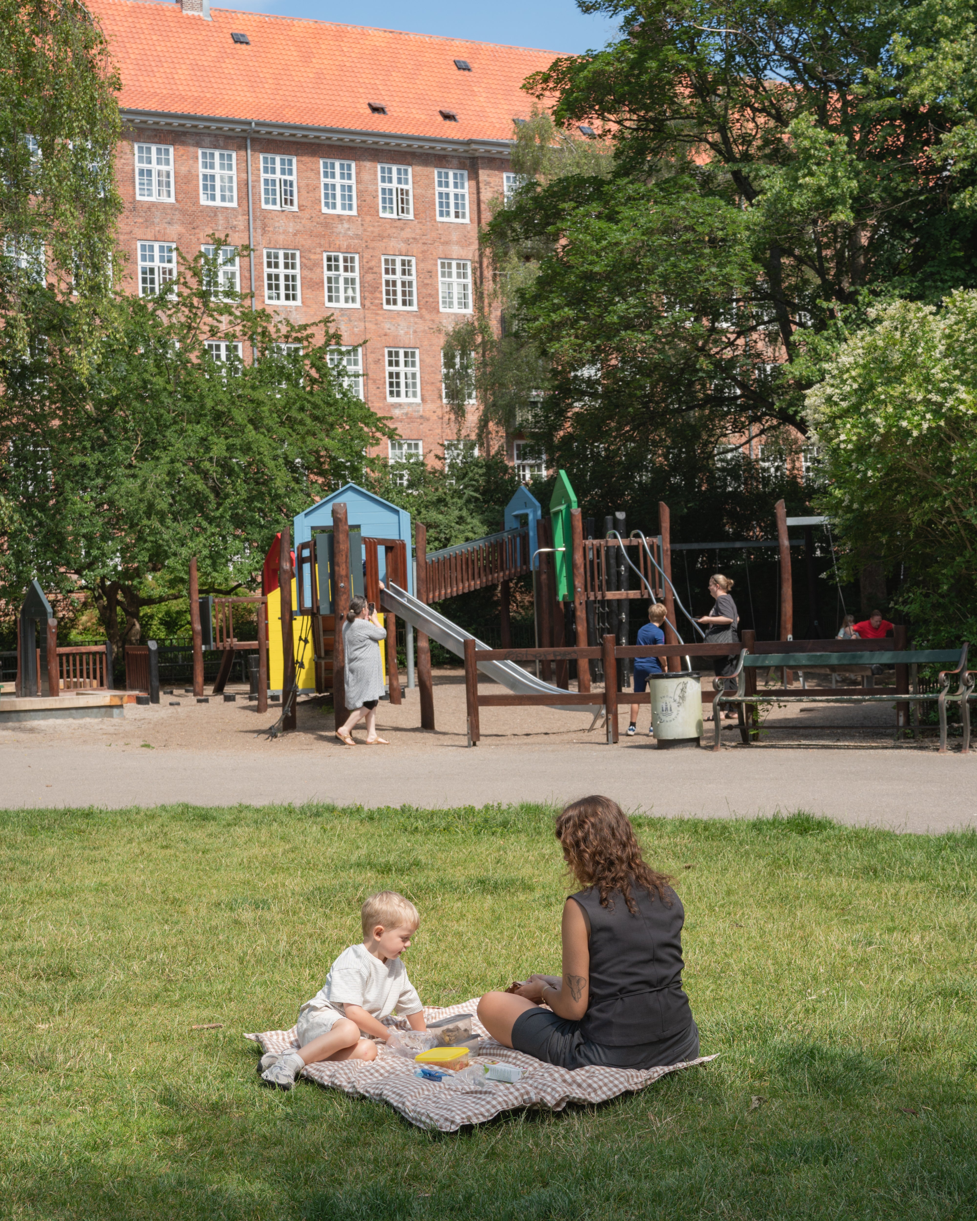 Woman and child sitting on a blanket in a park with playground in the background