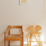 Two wooden chairs, one with a woven seat, against a white wall with a colorful abstract painting.