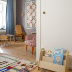 Children's room with wooden bookshelf, colorful rug, and chairs.