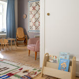 Children's room with wooden bookshelf, colorful rug, and chairs.
