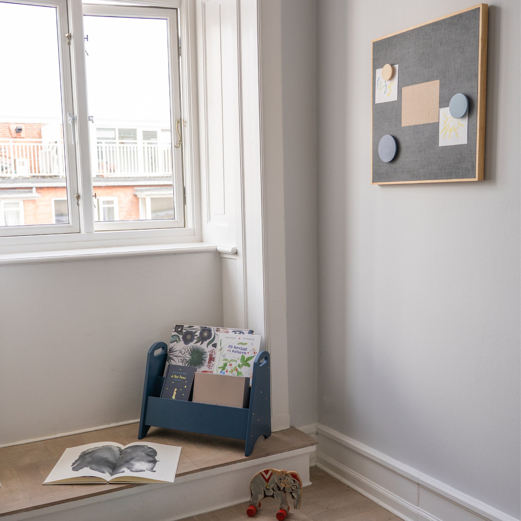 Nook with a window, magazine rack, books, and a toy on a wooden ledge.