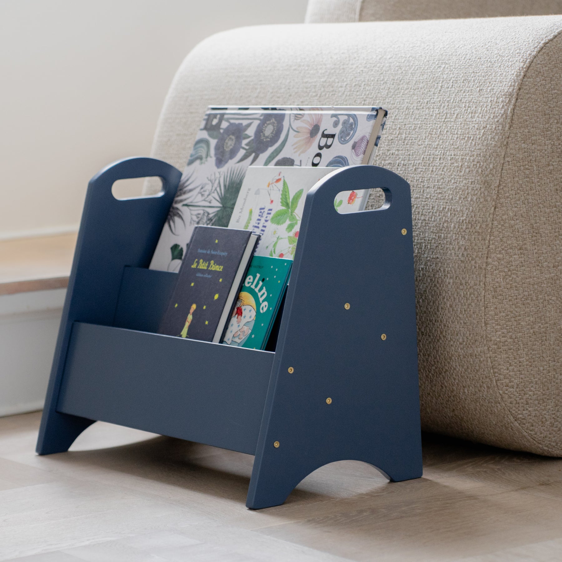Blue magazine rack with books and magazines on a beige couch