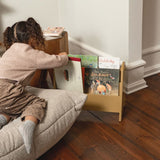 Child sitting on a couch next to a bookshelf with books