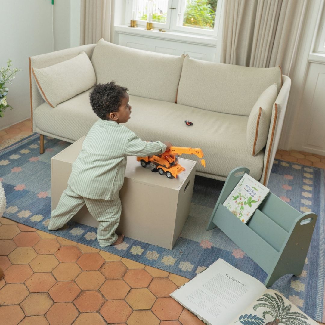 Child playing with toys on a small table in a room with a beige sofa and a window.