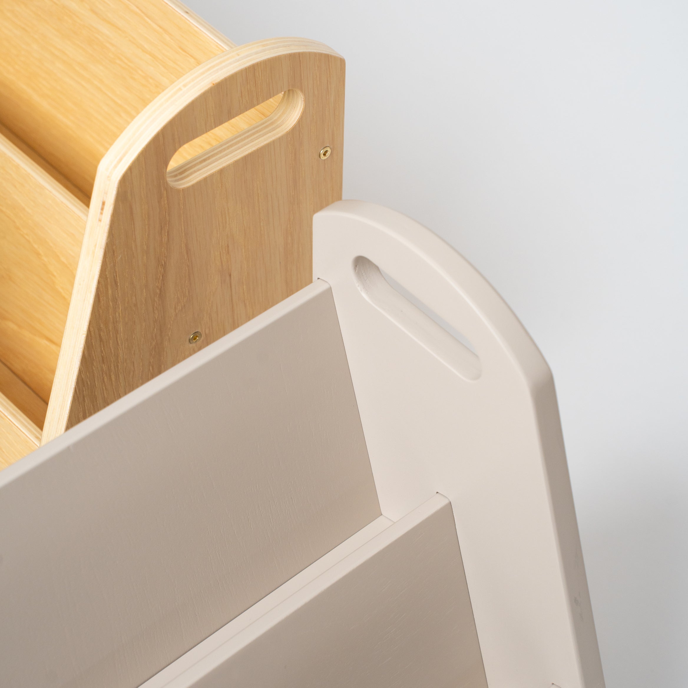 Close-up detail of a modern storage unit or bookshelf, showing a light beige plastic tiered section with a handle cutout next to a natural wood slatted section on a light gray background.