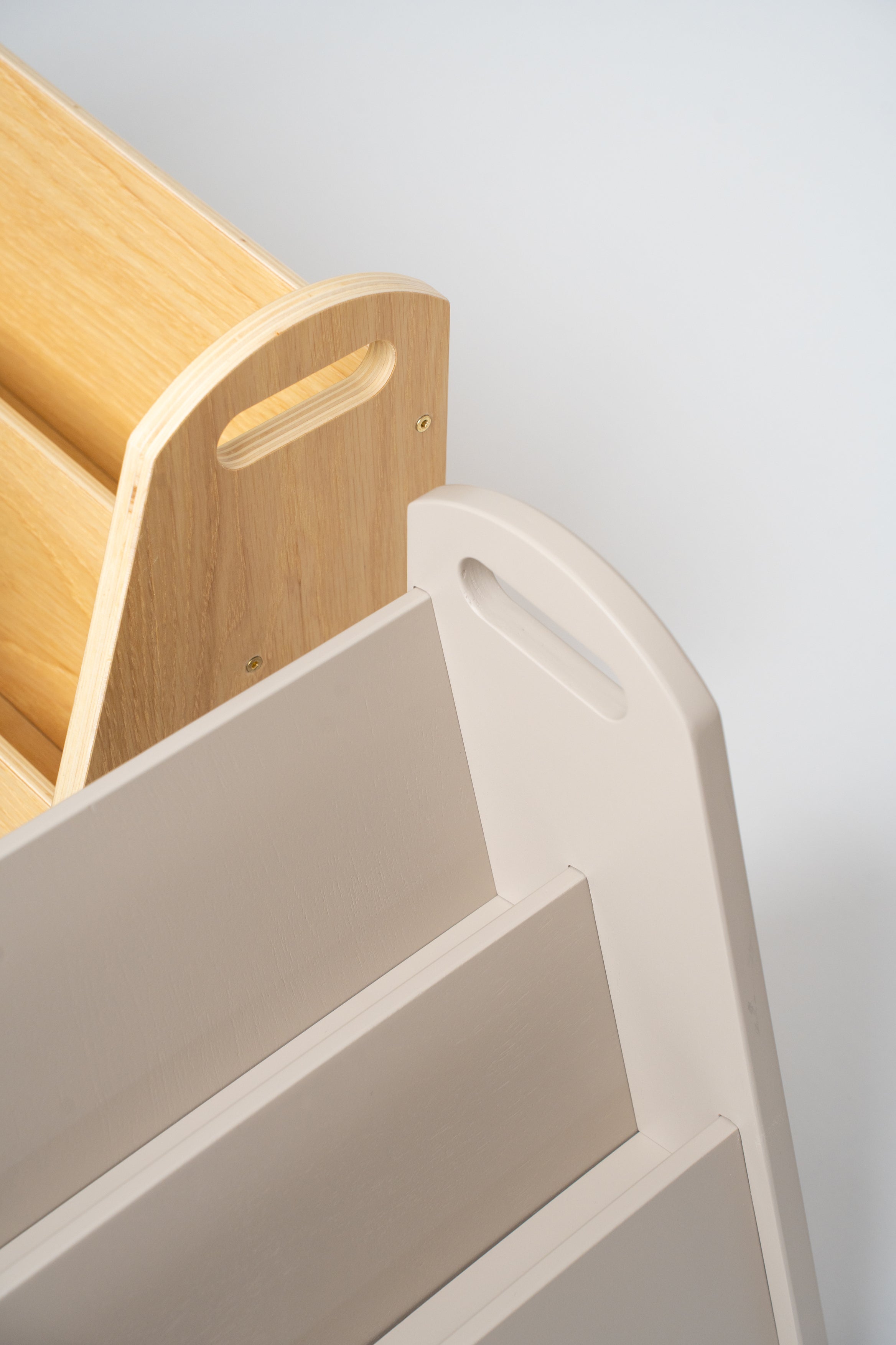 Close-up detail of a modern storage unit or bookshelf, showing a light beige plastic tiered section with a handle cutout next to a natural wood slatted section on a light gray background.