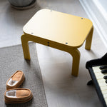 Curry step stool on a carpeted floor next to a piano and slippers.