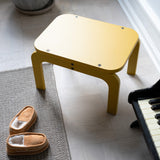Curry step stool on a carpeted floor next to a piano and slippers.