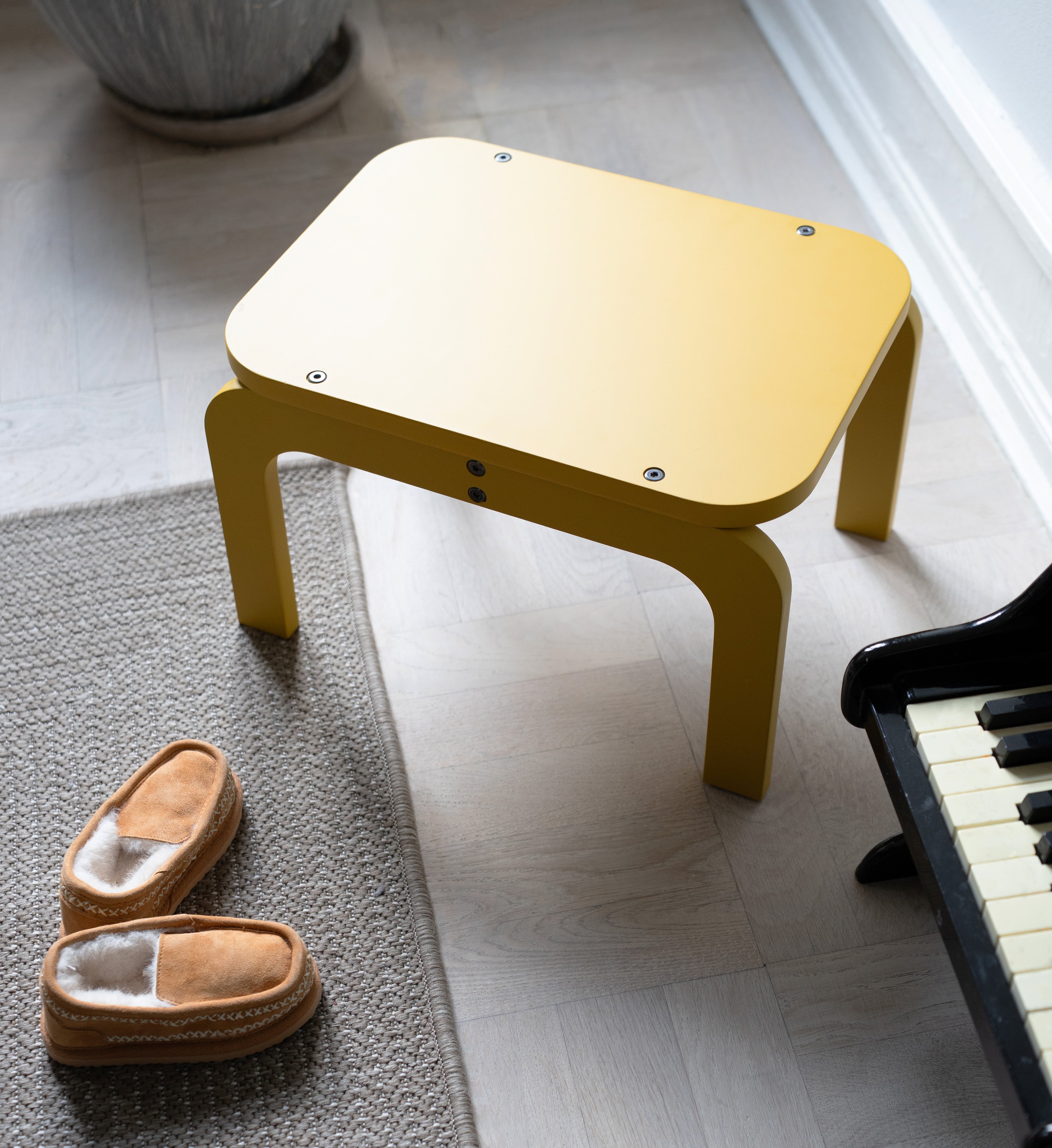 Curry step stool on a carpeted floor next to a piano and slippers.
