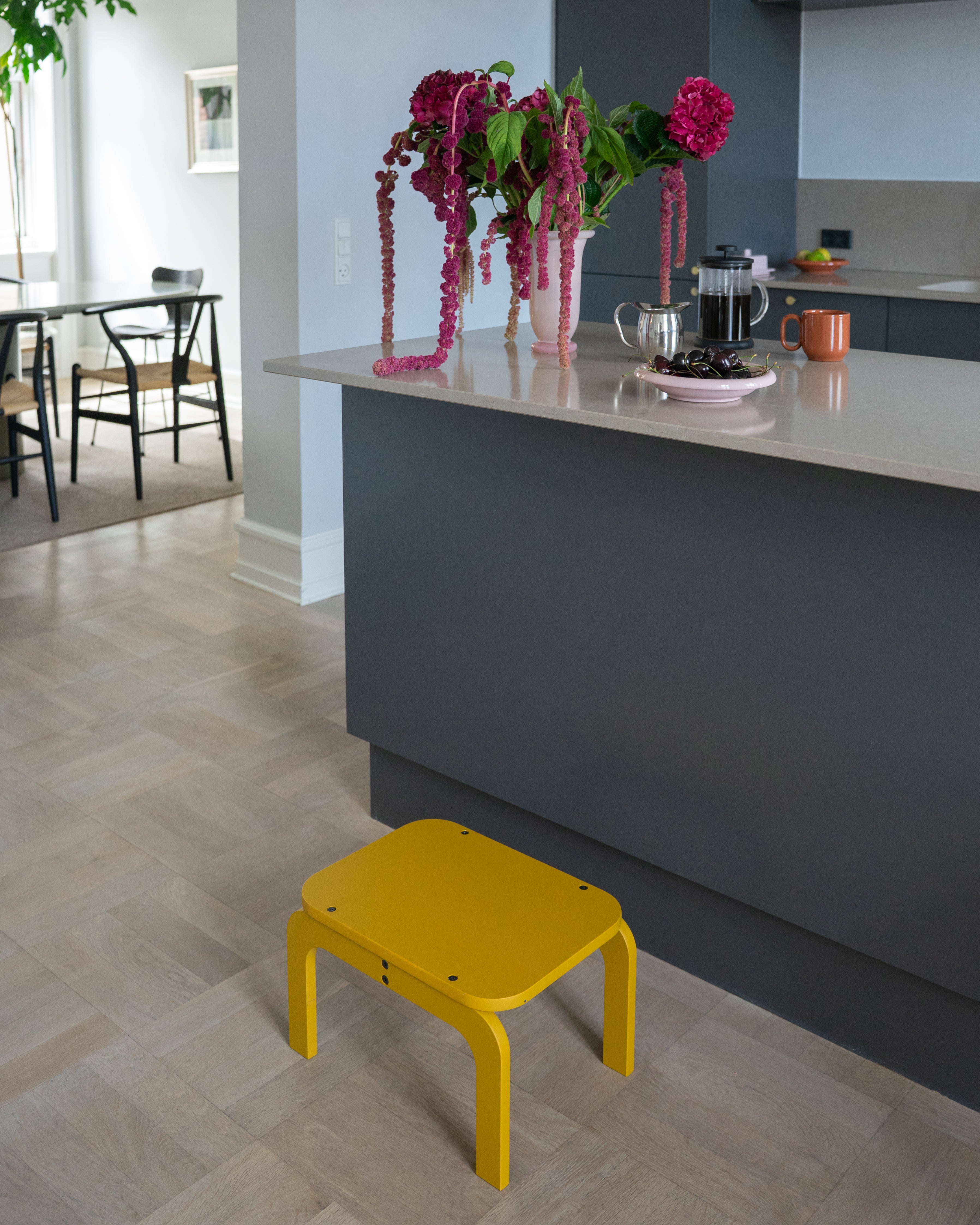 Curry step stool in a modern kitchen with a gray island and floral arrangement.