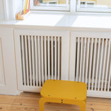 Curry stool in front of a white radiator with a window in the background