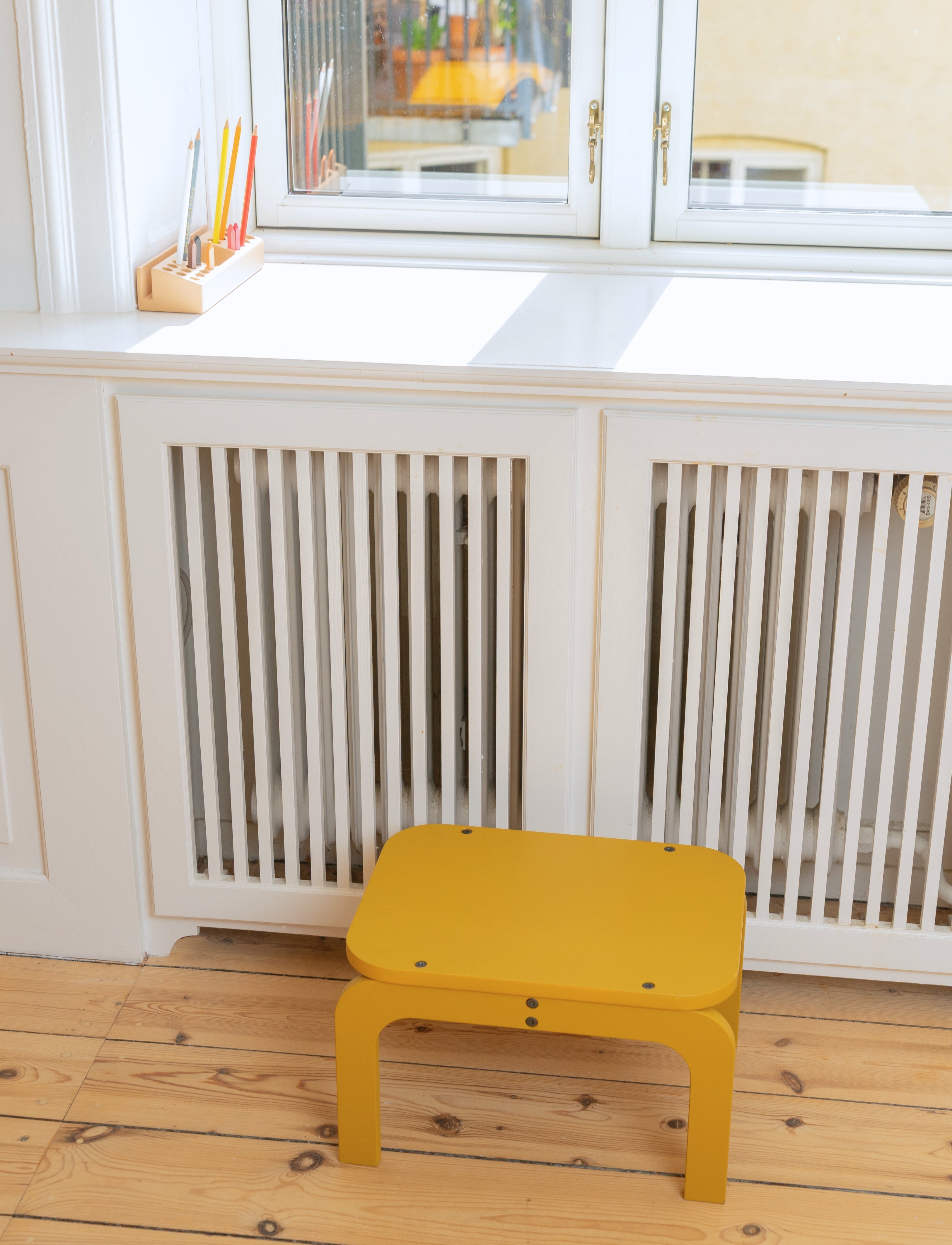 Curry stool in front of a white radiator with a window in the background