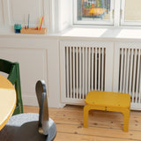 Children's room with a curry stool, green chair, and wooden table near a window.