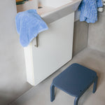 Bathroom with a white sink, blue towel, and a blue stool.
