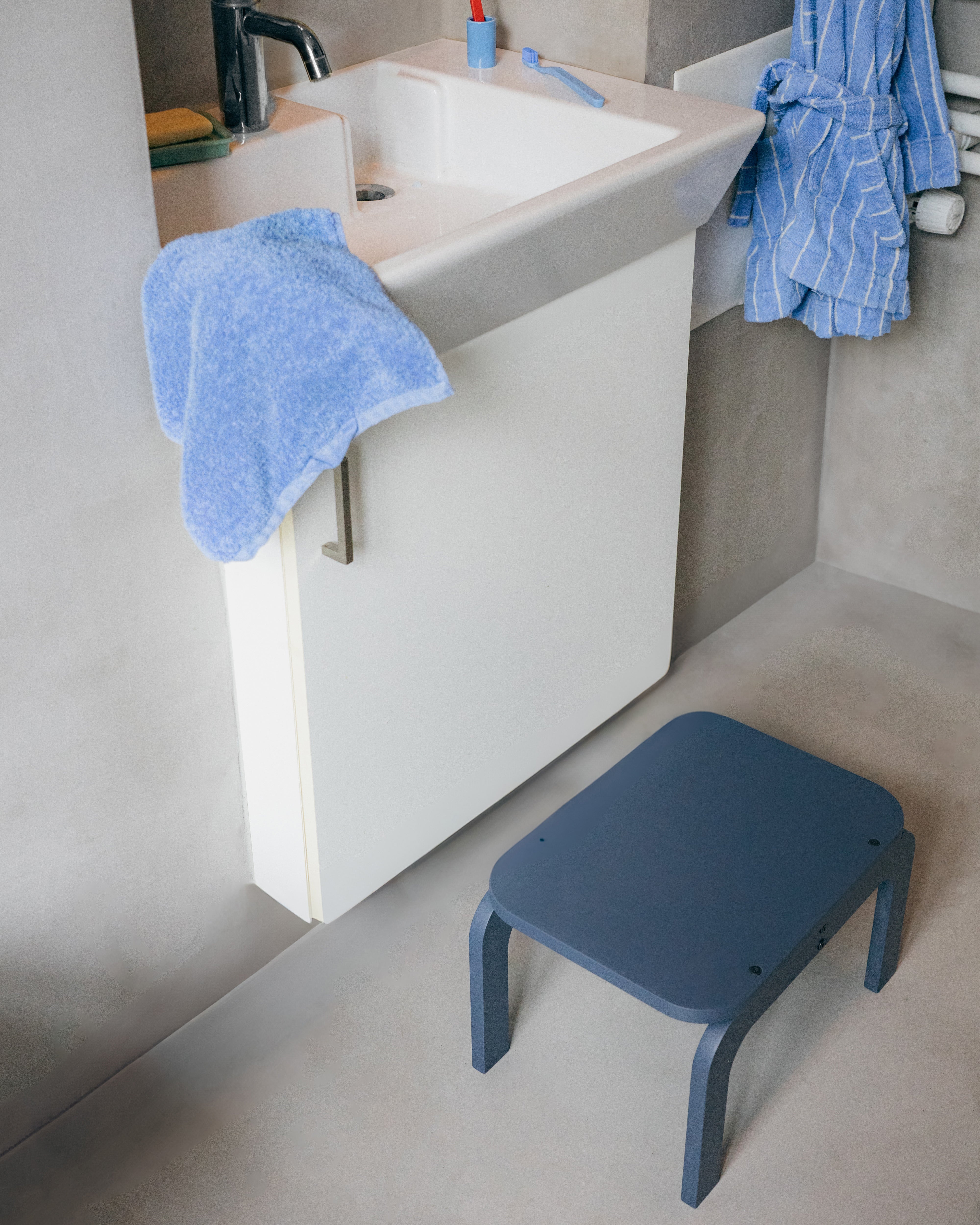 Bathroom with a white sink, blue towel, and a blue stool.