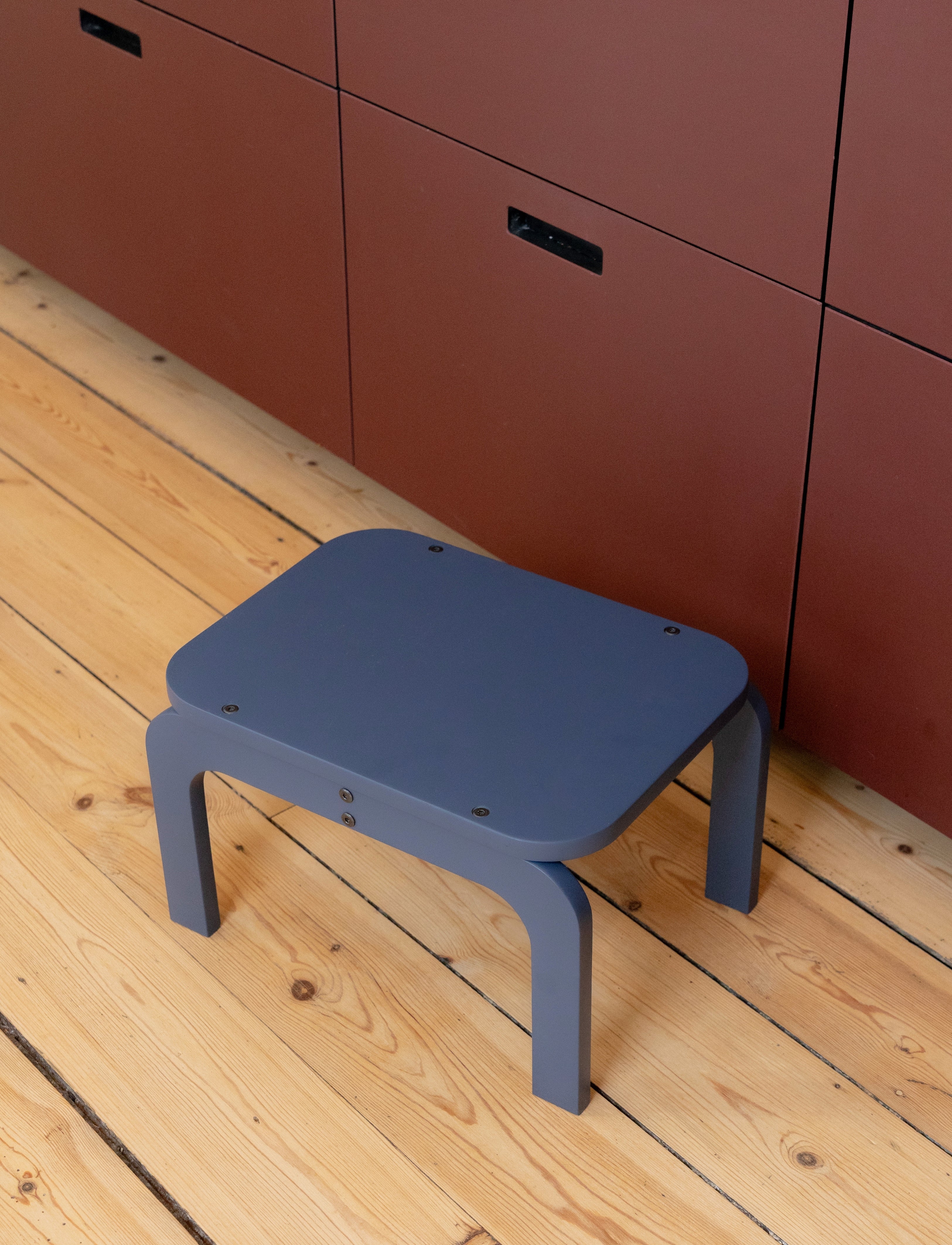 Blue stool on a wooden floor with red cabinets in the background