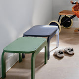 Two children's stools in green and blue on a wooden floor with a bicycle in the background.