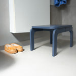 Blue stool next to a white cabinet with orange shoes on a light gray floor.