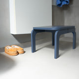 Blue stool next to a white cabinet with orange shoes on a light gray floor.