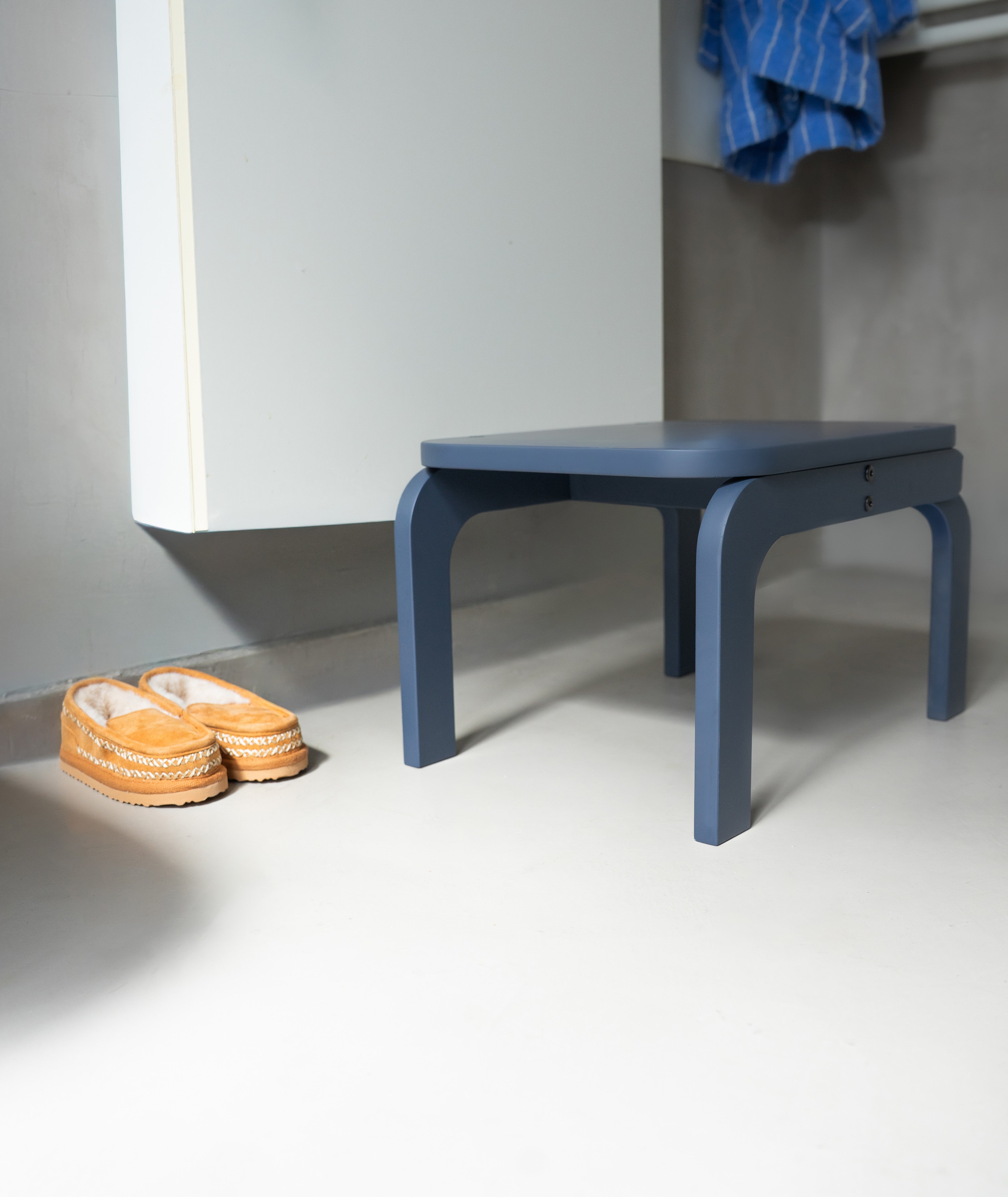 Blue stool next to a white cabinet with orange shoes on a light gray floor.
