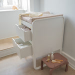 White changing table with drawers and a small brown table with baby care items in a room.