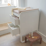 White changing table with drawers and a small brown table with baby care items in a room.