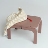 Children's table with a striped cloth and red toy on a light gray background