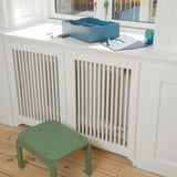 Green step stool in front of a white radiator with a window in the background