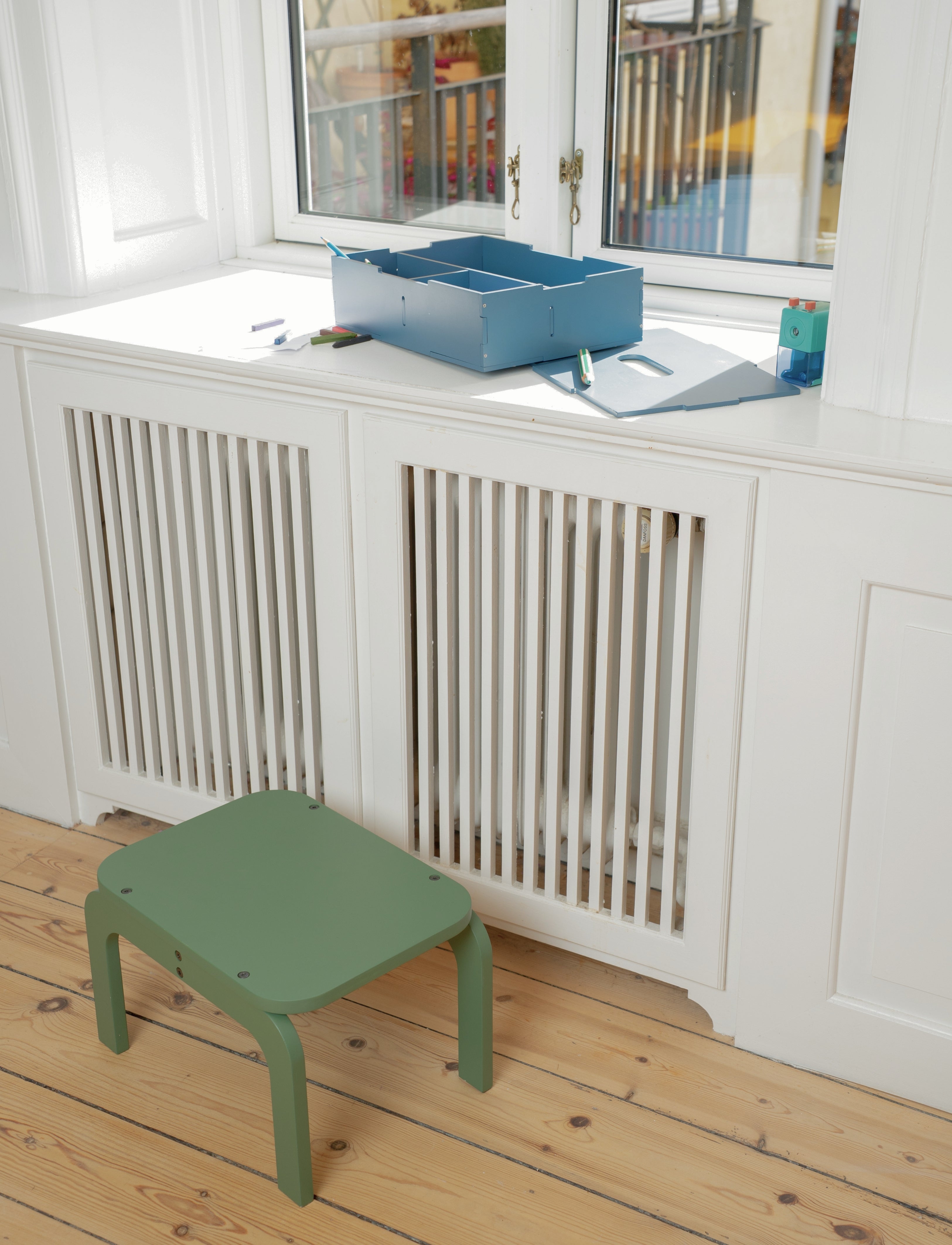 Green step stool in front of a white radiator with a window in the background
