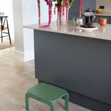 Green step stool in a kitchen setting with flowers and a coffee maker.