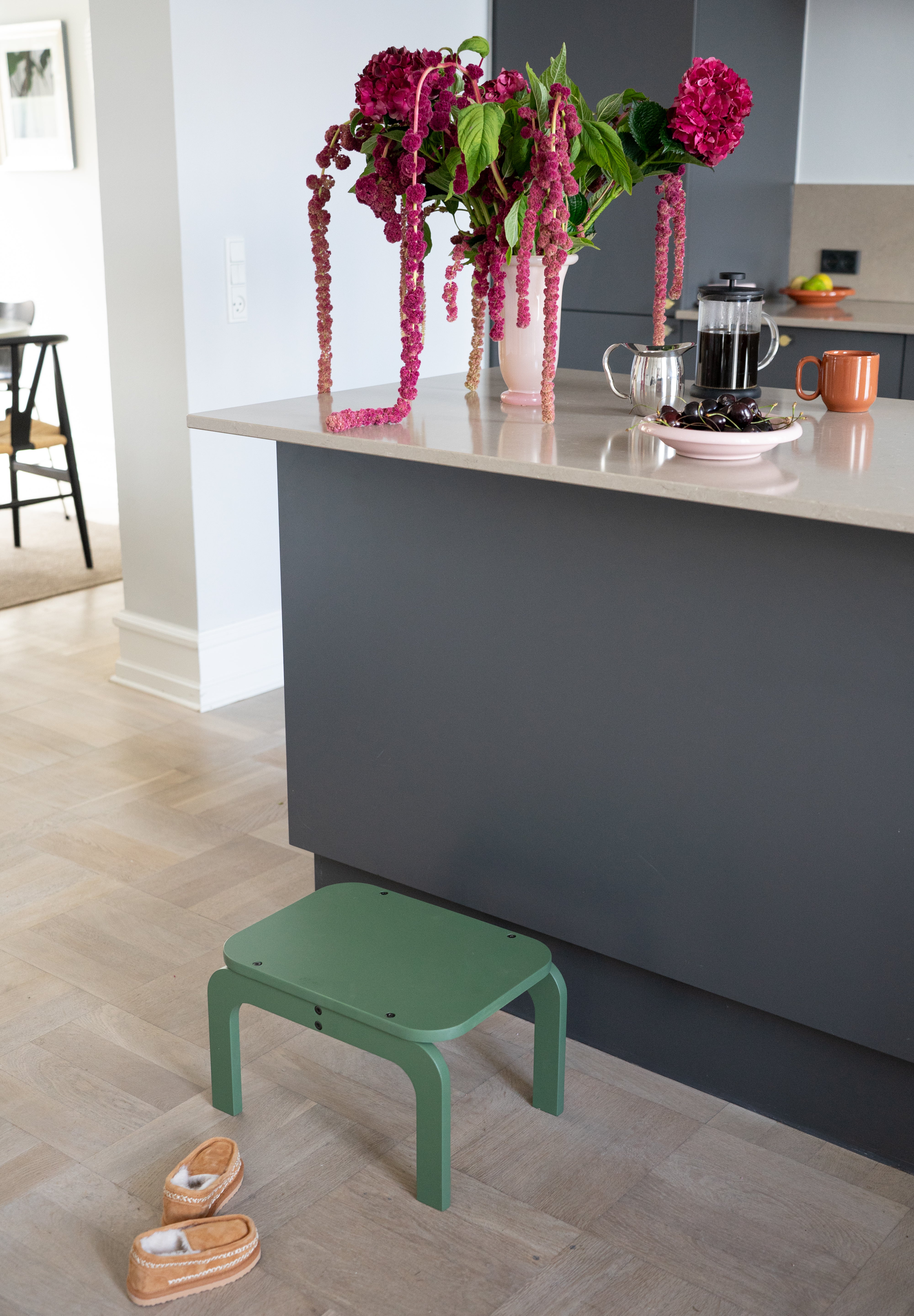 Green step stool in a kitchen setting with flowers and a coffee maker.