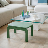 Green stool in front of a glass coffee table with stationery on a wooden floor.
