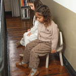 Two children sitting on a wooden floor in a room with books on a shelf.