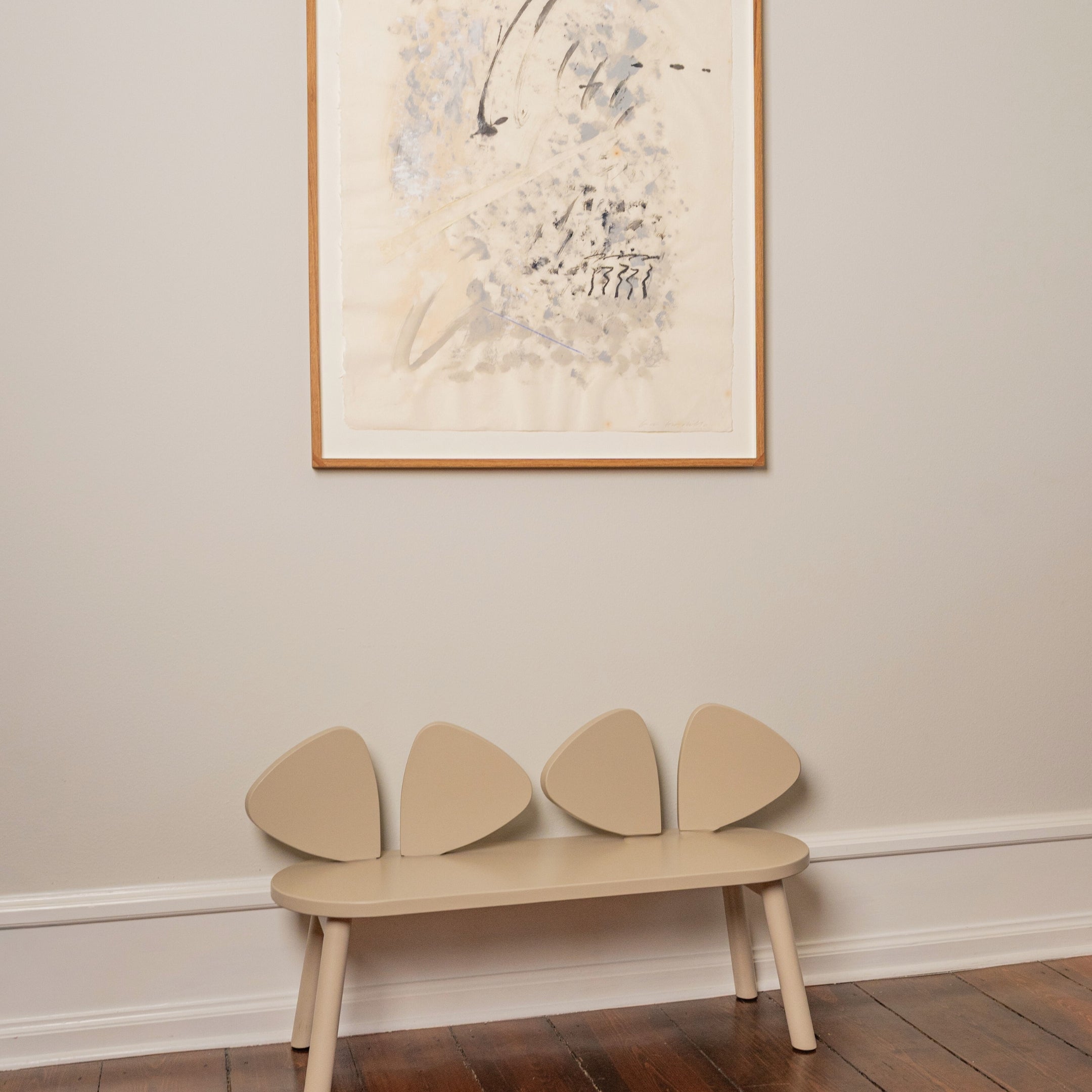 Beige bench with ear design against a wall with a framed picture