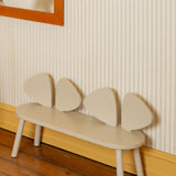 A minimalist children's bench with a curved cream-colored seat and four wing-like backrest panels, set against a striped wallpaper wall with a wooden floor.