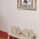 A cream-colored wooden bench with three curved backrests, placed against a patterned wallpaper wall with a framed art print above it.