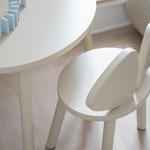 A close-up of a white children's table and matching chair in a bright, modern room with light wood flooring.