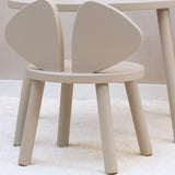A minimalist light beige children's chair with a rounded circular seat and two large, curved backrest panels, shown on a white textured rug.