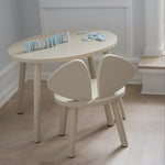 A minimalist children's table and chair set in a light cream or off-white finish, styled in a bright room with a light wood floor and white walls.