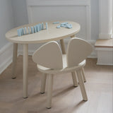 A minimalist children's table and chair set in a light cream or off-white finish, styled in a bright room with a light wood floor and white walls.