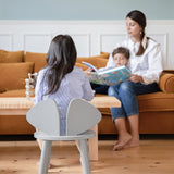 A girl sitting on the grey wooden chair with her mom and brother in front of her