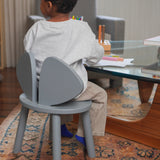 Child sitting on a gray chair at a glass table with colorful crayons.