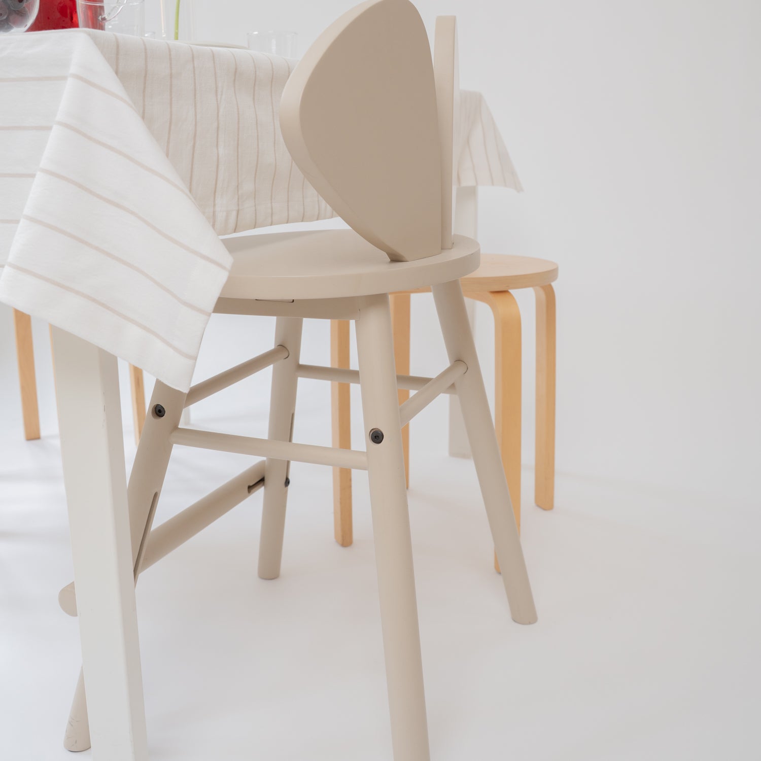 A light beige wooden dining chair with a curved backrest, shown in a bright, minimalist dining room setting alongside other wooden furniture.