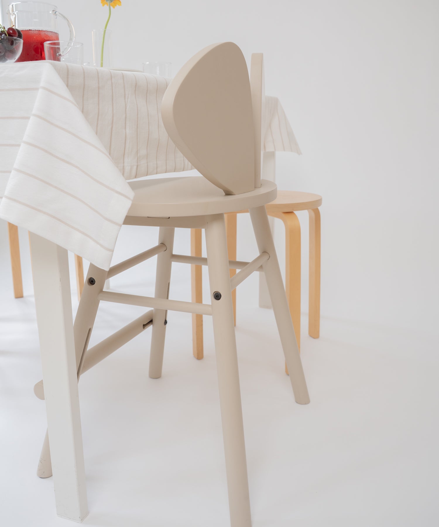 A light beige wooden dining chair with a curved backrest, shown in a bright, minimalist dining room setting alongside other wooden furniture.