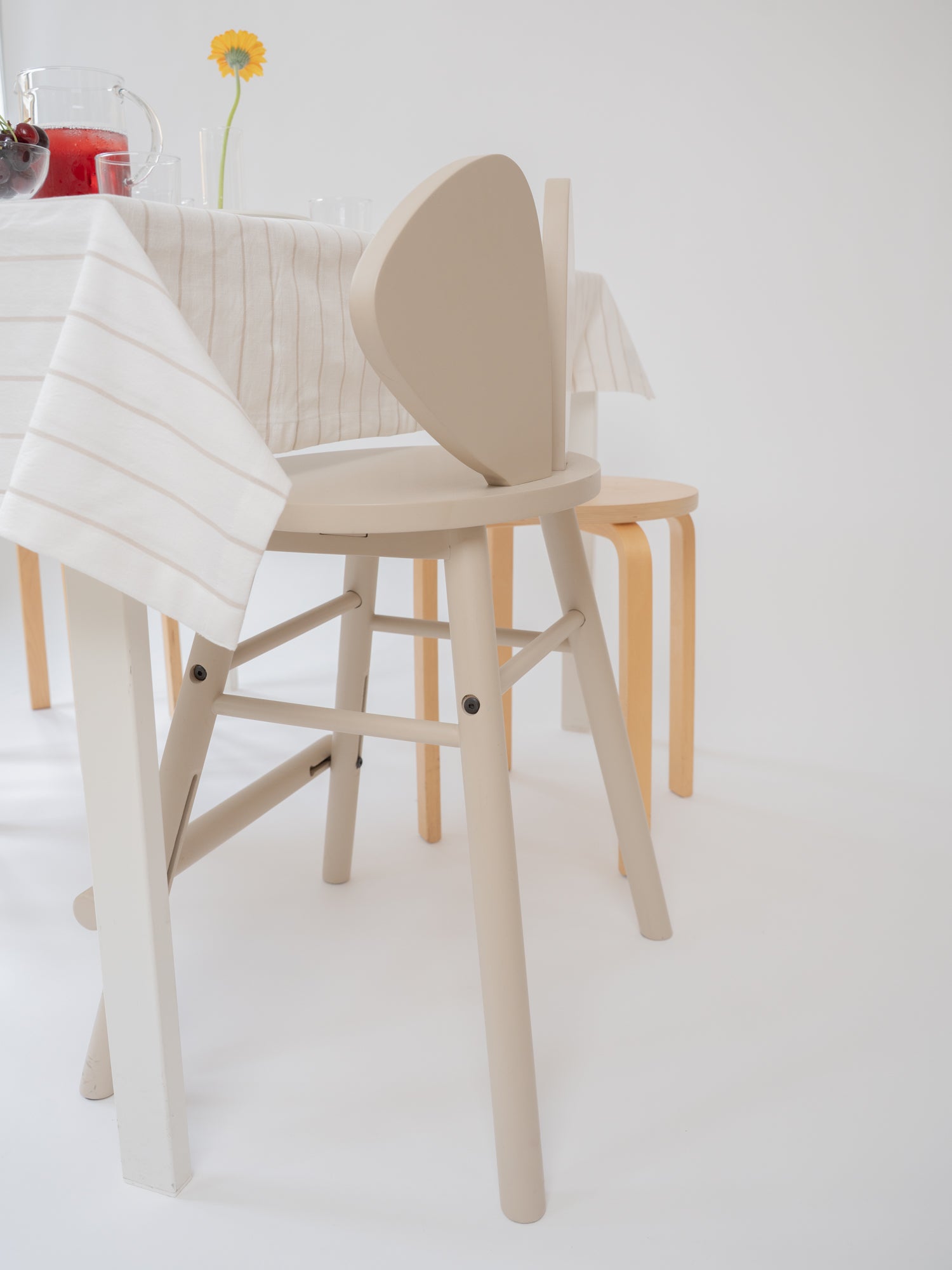 A light beige wooden dining chair with a curved backrest, shown in a bright, minimalist dining room setting alongside other wooden furniture.