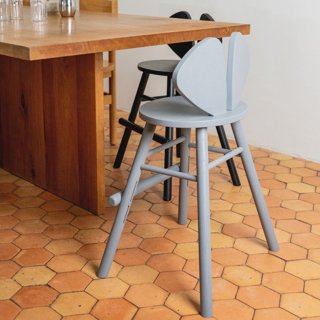 Gray stools in front of a wooden table on a hexagonal tiled floor.